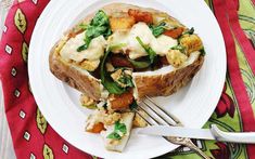 a white plate topped with a baked potato covered in cheese and vegetables next to a fork