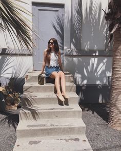 a woman is sitting on some steps with her suitcase in front of the door and palm trees