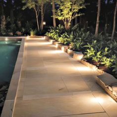 an outdoor walkway lit up at night next to a swimming pool with trees in the background