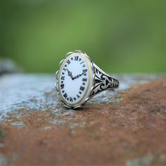 a white and gold ring with roman numerals sits on a piece of stone