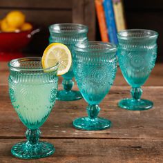 three green glass goblets sitting on top of a wooden table with lemons in the background