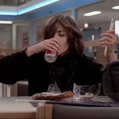 a woman sitting at a table drinking from a can