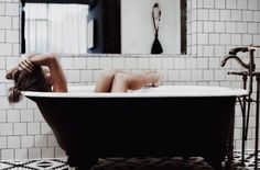 a woman laying in a bathtub with her head on the back of the tub