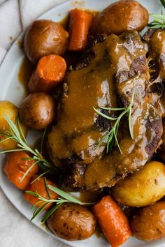 a white plate topped with meat and potatoes covered in gravy next to carrots