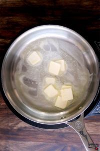 cubed cheese being cooked in a saucepan on a stove top with a measuring spoon