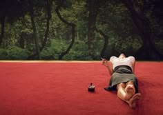 a man laying on the ground in front of a red carpet with trees behind him