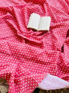 an open book laying on top of a bed covered in pink sheets and polka dots