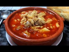 there is a bowl of soup on the table next to some bread and spoons