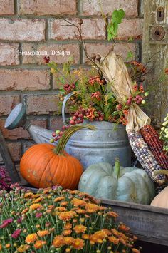 pumpkins, gourds and other autumn flowers are arranged in front of a brick wall