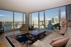 a living room filled with furniture and large windows overlooking the cityscape in the distance