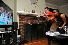 two men playing video games in front of a fireplace