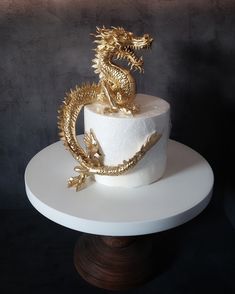 a white cake with gold dragon decorations on the top and bottom, sitting on a pedestal