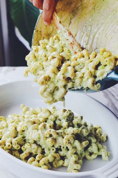 a person pouring macaroni and cheese into a white bowl on top of a table