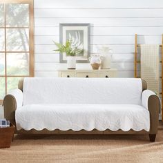 a white couch sitting in a living room next to a wooden table and dresser with a potted plant on top of it