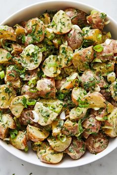 a white bowl filled with potato salad on top of a marble countertop and topped with parsley