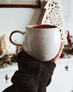 a hand holding a white and brown coffee cup in front of a christmas tree ornament