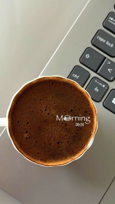 a cup of coffee sitting on top of a laptop keyboard