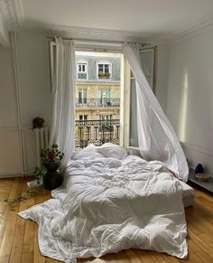 an unmade bed sitting on top of a hard wood floor next to a window