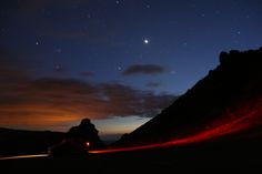 a car driving down a road at night with the moon in the sky above it