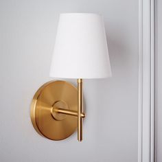 a gold wall light with a white shade on it's side and a door in the background