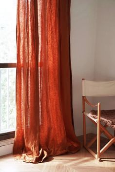 an orange sheer curtain hanging in front of a window next to a chair and table