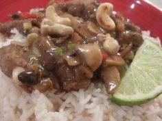 a red plate topped with rice and meat covered in mushroom sauce next to a slice of lime