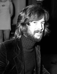 a man with long hair and beard wearing a black turtle neck sweater sitting in front of a woman