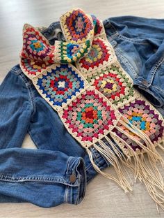 a crocheted scarf laying on top of denim pants and a pair of jeans