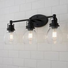 three light bathroom fixture with clear glass globes and black metal fixtures on the wall