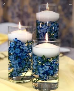 three candles with blue flowers in them on a table