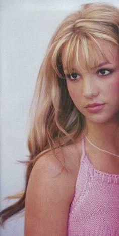 a woman with long blonde hair wearing a pink tank top and looking at the camera