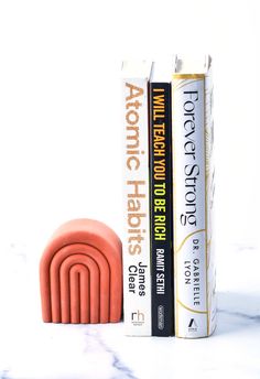 two books are sitting next to each other on a marble counter top with an orange bookend