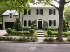 a large white house with black shutters and green trees in front of the house