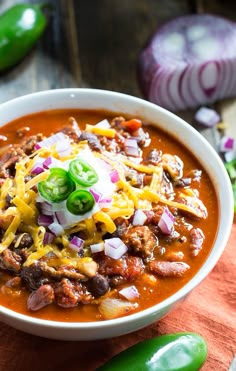 a white bowl filled with chili and cheese on top of a wooden table next to onions