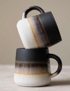 two coffee mugs stacked on top of each other in black and white cups with brown stripes