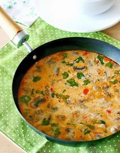 thai spicy coconut soup in a skillet on a green place mat next to a cup of coffee