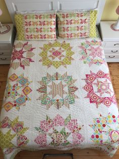 a bed with a colorful quilt on top of it next to a night stand and nightstand