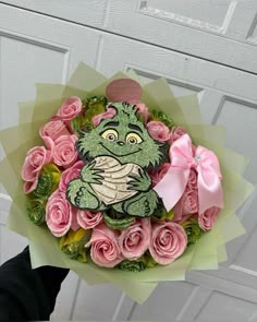 a hand holding a bouquet of pink roses with a green frog on it's face