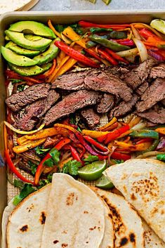 a tray filled with meat and veggies next to tortillas