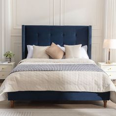 a bed with blue headboard and pillows in a white walled room, along with two nightstands