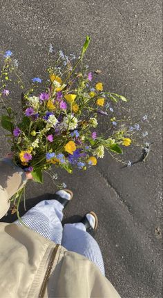 a person holding a bouquet of flowers in their hand on the ground next to asphalt