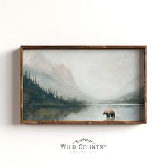 a painting hanging on the wall with a bear in it's frame next to a mountain lake