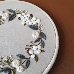 a white embroidered circle with flowers and leaves around it on a brown table cloth covered surface