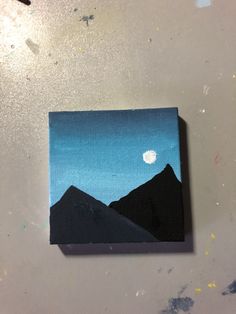 a painting on a table with mountains and a moon in the sky behind it,