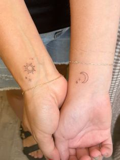 two people holding hands with small tattoos on their wrist and the sun and moon behind them