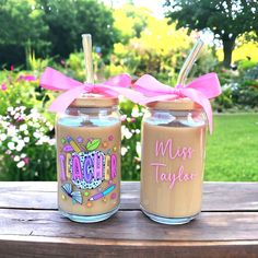 two personalized mason jars with straws in them on a wooden table outside near flowers