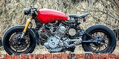 a red and black motorcycle parked on top of a brick wall in front of trees