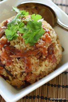 rice with sauce and parsley on top in a square white bowl next to a spoon