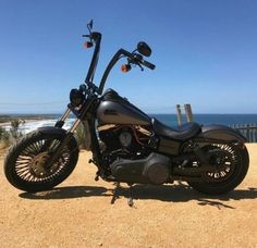 a black motorcycle parked on top of a dirt road next to the ocean and beach