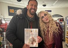 a man and woman standing next to each other in a store holding up a magazine